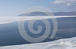 Baikal lake spring landscape view. Snow-covered shore of the lake. Rocky forested coastline. Boundary of ice and open