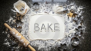 Bake word in flour with baking tools on dark background