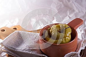 A baked apple in a clay pot on a linen cloth and wooden desk against white background