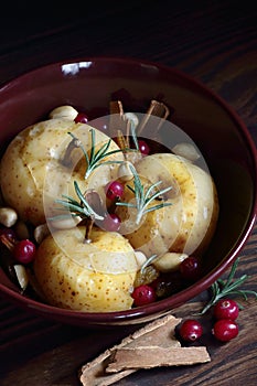 Baked apples, autumn or christmas winter dessert with cranberries, cinnamon, nuts and rosemary on dark moody background