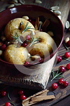 Baked apples, autumn or christmas winter dessert with cranberries, cinnamon, nuts and rosemary on dark moody background