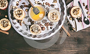 Baked apples with nuts and honey on a round baking tray on a wooden background, top view