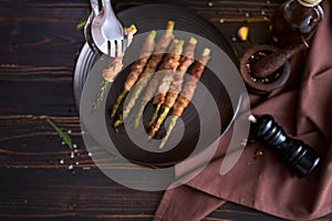 baked aspargus covered with bacon on a black ceramic plate on wooden kitchen table