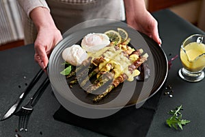 baked aspargus covered with bacon and poached eggs on a black ceramic plate