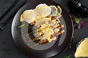 baked aspargus covered with bacon and poached eggs on a black ceramic plate