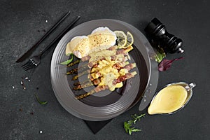 baked aspargus covered with bacon and poached eggs on a black ceramic plate