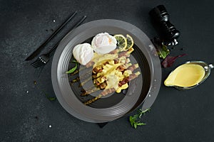 baked aspargus covered with bacon and poached eggs on a black ceramic plate