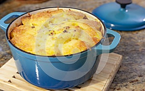 Baked Au Gratin potateos in blue cast iron baking pot with melted cheese on top