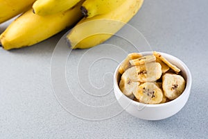 Baked banana chips in a white bowl and a bunch of bananas on the table. Fast food. Close-up. Vertical view. Copy space