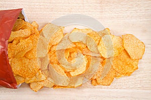 Baked BBQ potato chips spilling from bag on light wood table