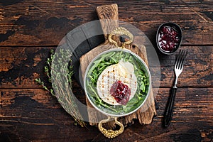 Baked Camembert Brie cheese with a cranberry sauce and garnished with arugula salad in a skillet. Wooden background. Top