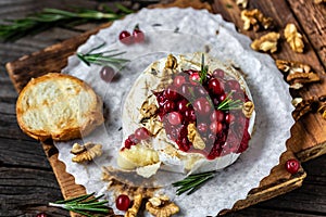 Baked camembert with cranberry sauce, baguette bread and rosemary on rustic wooden table