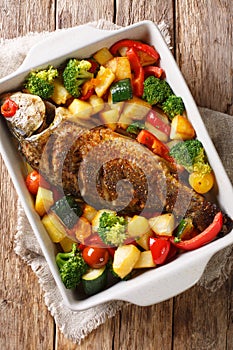 Baked carp with vegetables close-up in a baking dish. Vertical top view