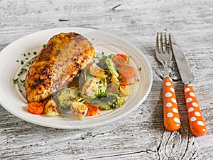 Baked chicken breast with brussels sprouts, onions and carrots on a white plate on wooden surface.