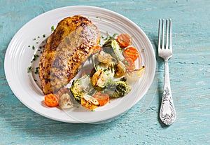 Baked chicken breast with brussels sprouts, onions and carrots on a white plate on wooden surface.