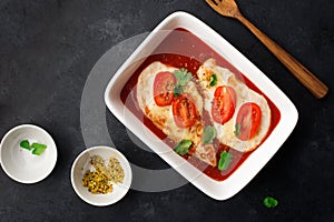 Baked chicken breast with cheese and tomato slices in a juicy tomato sauce on a baking sheet. Top view. Healthy eating,