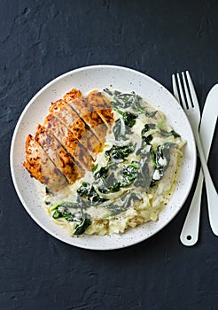 Baked chicken breast, mashed potatoes with creamy spinach on dark background, top view