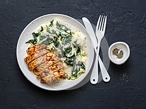 Baked chicken breast, mashed potatoes with creamy spinach on dark background, top view.