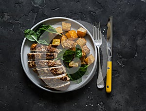 Baked chicken breast, pumpkin and spinach - a delicious healthy lunch on a dark background, top view