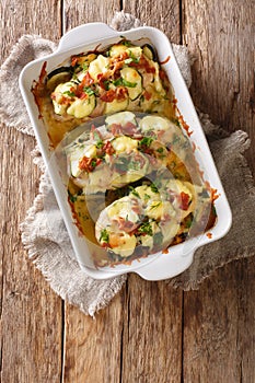 Baked chicken breast with zucchini, bacon and cheese close-up in a baking dish. vertical top view