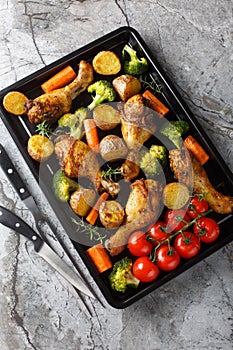 Baked chicken drumstick with broccoli, potatoes, tomatoes, and carrots close-up on a sheet pan. Vertical top view