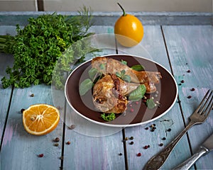 Baked chicken drumsticks with fresh parsley sprigs on a brown plate on a plain wooden tray