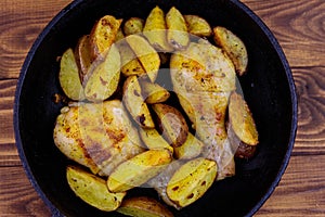 Baked chicken drumsticks with potatoes in in cast-iron frying pan on wooden table. Top view