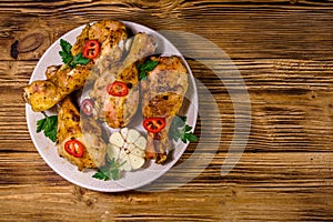 Baked chicken legs with parsley, garlic and sliced red hot pepper in a plate. Top view