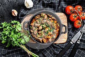 Baked chicken liver hearts in the cast iron pan. Black background. Top view