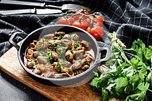 Baked chicken liver hearts in the cast iron pan. Black background. Top view