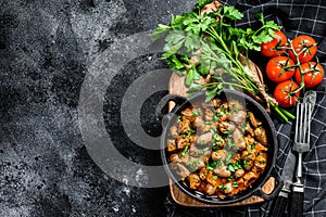 Baked chicken liver hearts in the cast iron pan. Black background. Top view. Copy space