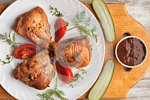 Baked chicken thighs, vegetables and sauce on a wooden background