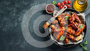 Baked chicken wings in barbecue sauce with sesame seeds and parsley in a cast iron pan on a dark concrete table. Top view with