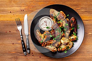 Baked chicken wings in Mexican with curry seasoning and parsley on a black plate, on a wooden background. side view, copy space