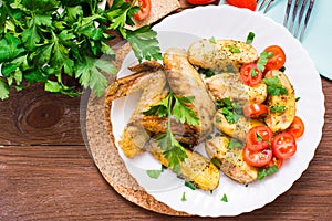 Baked chicken wings and potatoes, fresh tomatoes and greens