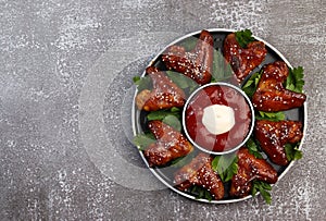 Baked chicken wings with sesame and sauce on a round plate on a dark background