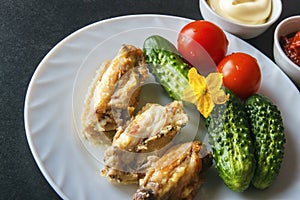 Baked chicken wings in tomato paste and mayonnaise on a white plate with fresh organic vegetables on a black background. Copy spac