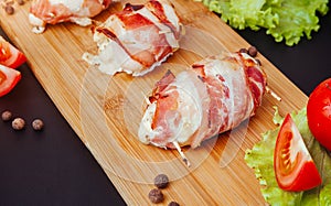 Baked chicken wrapped in bacon. Delicious appetizer with crispy smoked bacon. Chicken breast wrapped in bacon on wooden board.