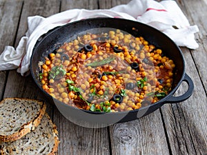 Baked chickpea Baked chickpea with vegetables, olives and sundried tomatoes in iron pan, frying pan on wooden table