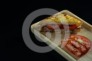 Baked croque monsieur spinach and ham sandwich with tomato on wood plate, isolated black background