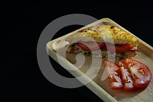 Baked croque monsieur spinach and ham sandwich with tomato on wood plate, isolated black background