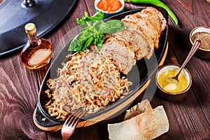 Baked dish of beef, noodles, rice, mushrooms, onions served with butter, spices and cognac in pan on wooden table.