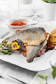 Baked Dorado fillet fish with sweet potato, lime and tomato sauce at the white plate on light marble background. Healthy sea food