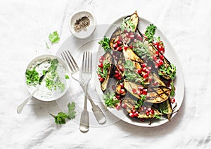 Baked eggplant with feta, greek yogurt, cilantro sauce and pomegranate seeds on light background, top view. Delicious snack, tapas