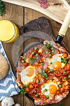 Baked eggs with chorizo, potatoes and tomatoes in a pan on the table. top view