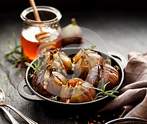 Baked figs stuffed with gorgonzola cheese, pine nuts, honey and herbs in a black dish on a dark, stone background, top view.