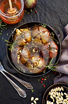 Baked figs stuffed with gorgonzola cheese, pine nuts, honey and herbs in a black dish on a dark, stone background, top view.