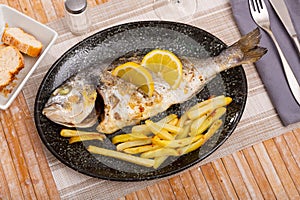 Baked fish called Dorada with French fries and lemon slices