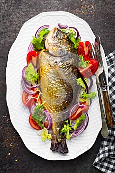 Baked fish dorado. Dorado fish oven baked and fresh vegetable salad on plate. Sea bream or dorada fish grilled and vegetable salad