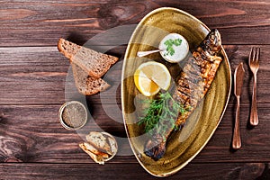 Baked fish with lemon and greens on plate on wooden background.